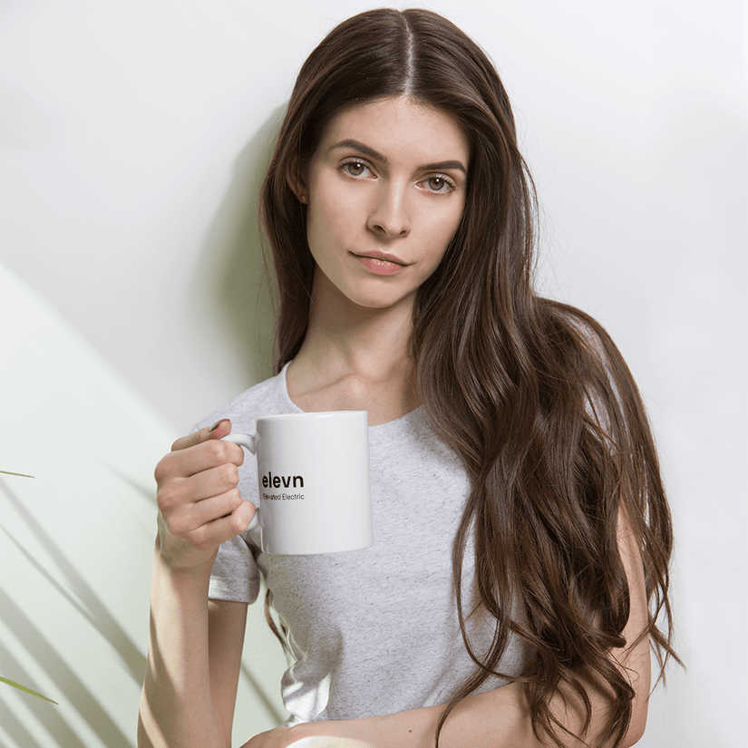 Hand holding a white elevnEV ceramic mug with Elevated Electric lockup in a cafe overlooking a city street at dusk